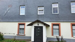 A two-story building with a dark grey roof, white window frames, and a black door. - Vacation apartment Lehesten Zinkenweg (Lehesten)
