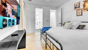 A modern hotel room with a large flat-screen TV mounted on the wall, a bed with white bedding, and a bedside table with a remote control.