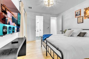 Ein modernes Hotelzimmer mit einem großen Flachbildfernseher an der Wand, einem Bett mit weißer Bettwäsche und einem Nachttisch mit Fernbedienung.