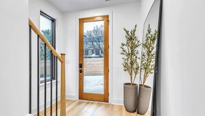 A modern hallway with a wooden staircase, a wooden door, and two large potted plants.
