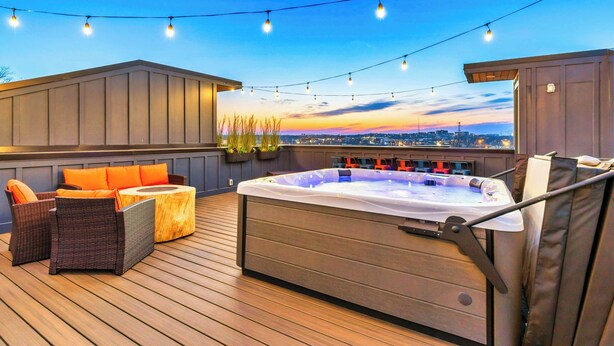 A rooftop deck with a hot tub, outdoor seating, string lights, and a city view.