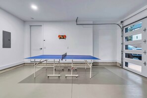 A ping pong table in a room with white walls, a garage door, and a small shelf with a clock.