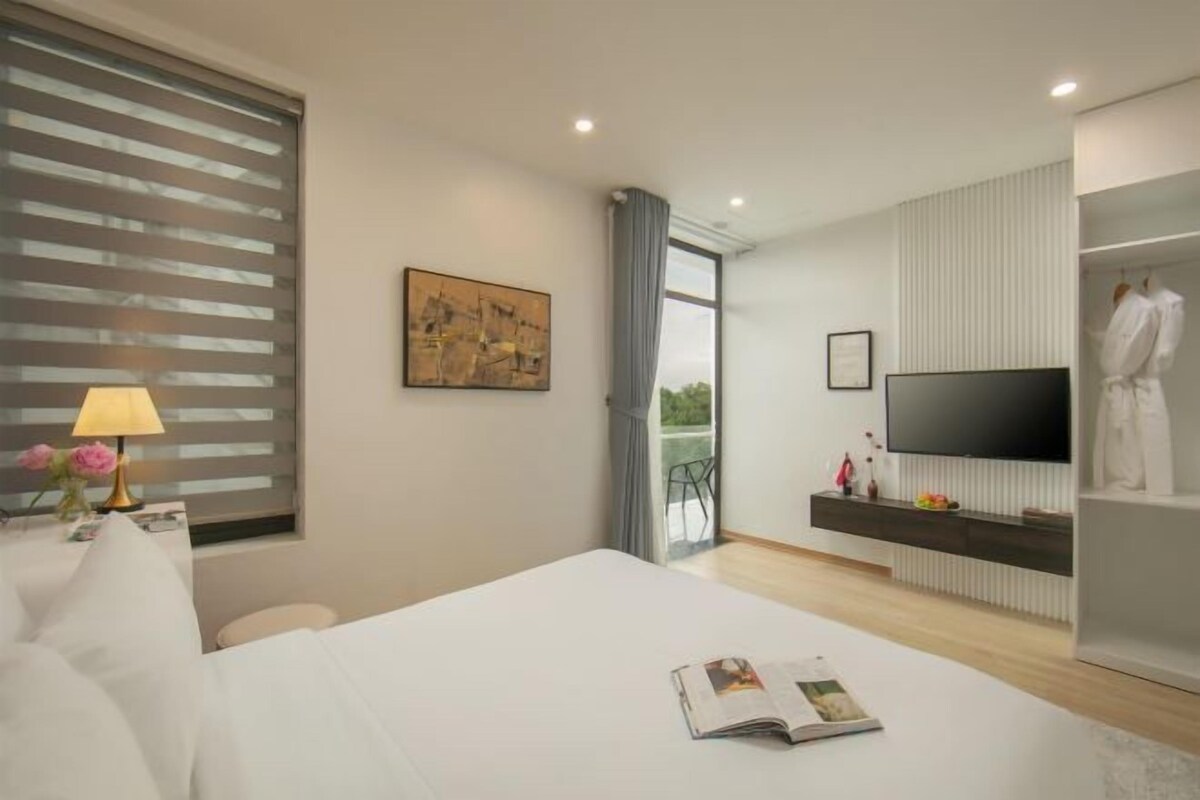 Une chambre d’hôtel moderne dotée d’un grand lit, d’un téléviseur à écran plat, d’une table de chevet avec une lampe et offrant une vue sur l’extérieur.
