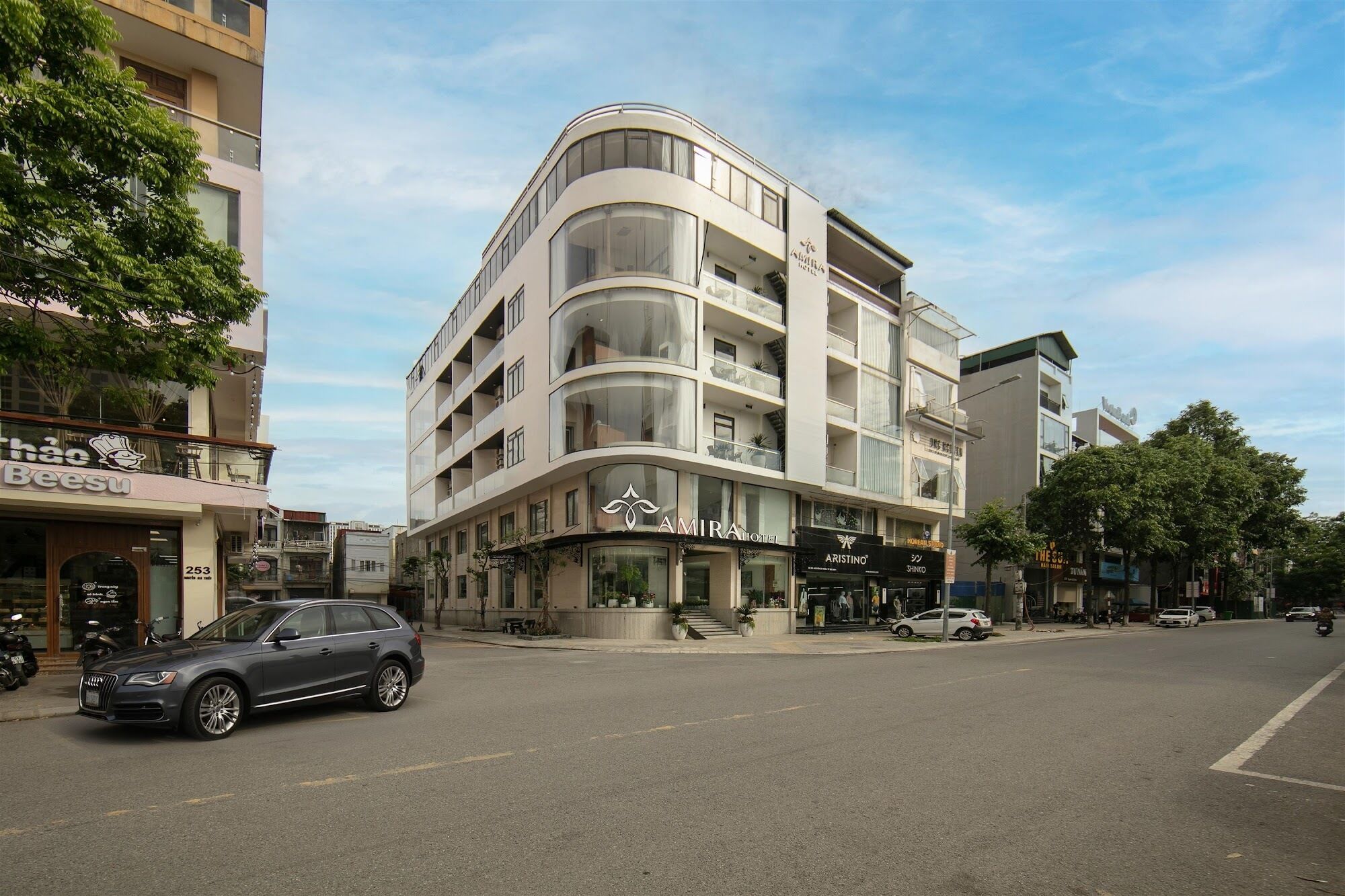 A modern hotel with a curved facade, multiple balconies, and a ground-level restaurant.