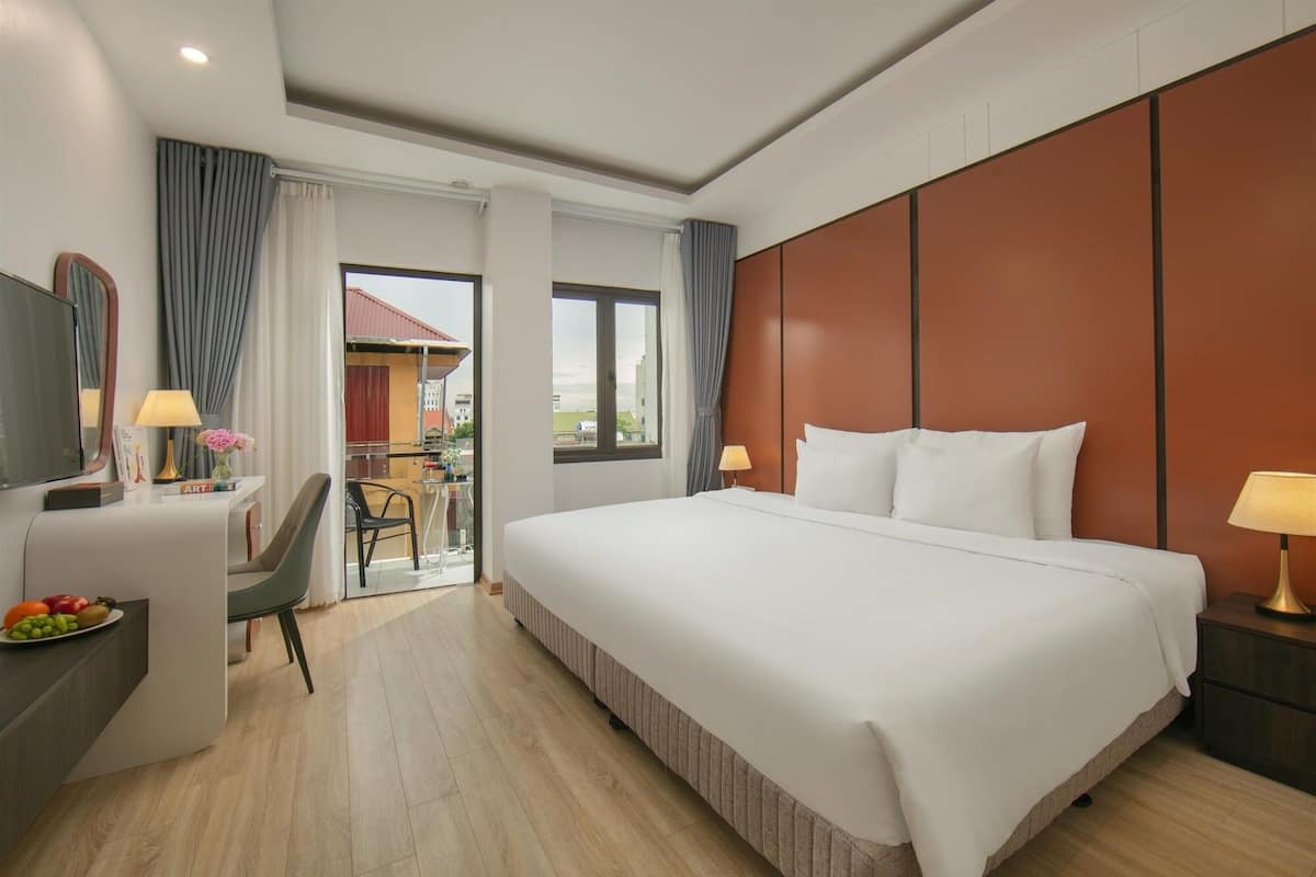 Une chambre d’hôtel avec un grand lit, un bureau avec une chaise, une télévision et un balcon donnant sur les bâtiments.