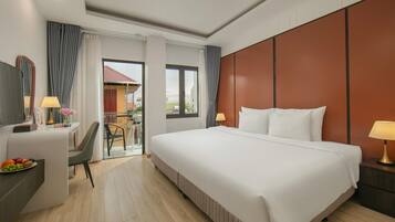 Habitación de hotel con una cama grande, un escritorio con una silla, televisión y balcón con vista a edificios.