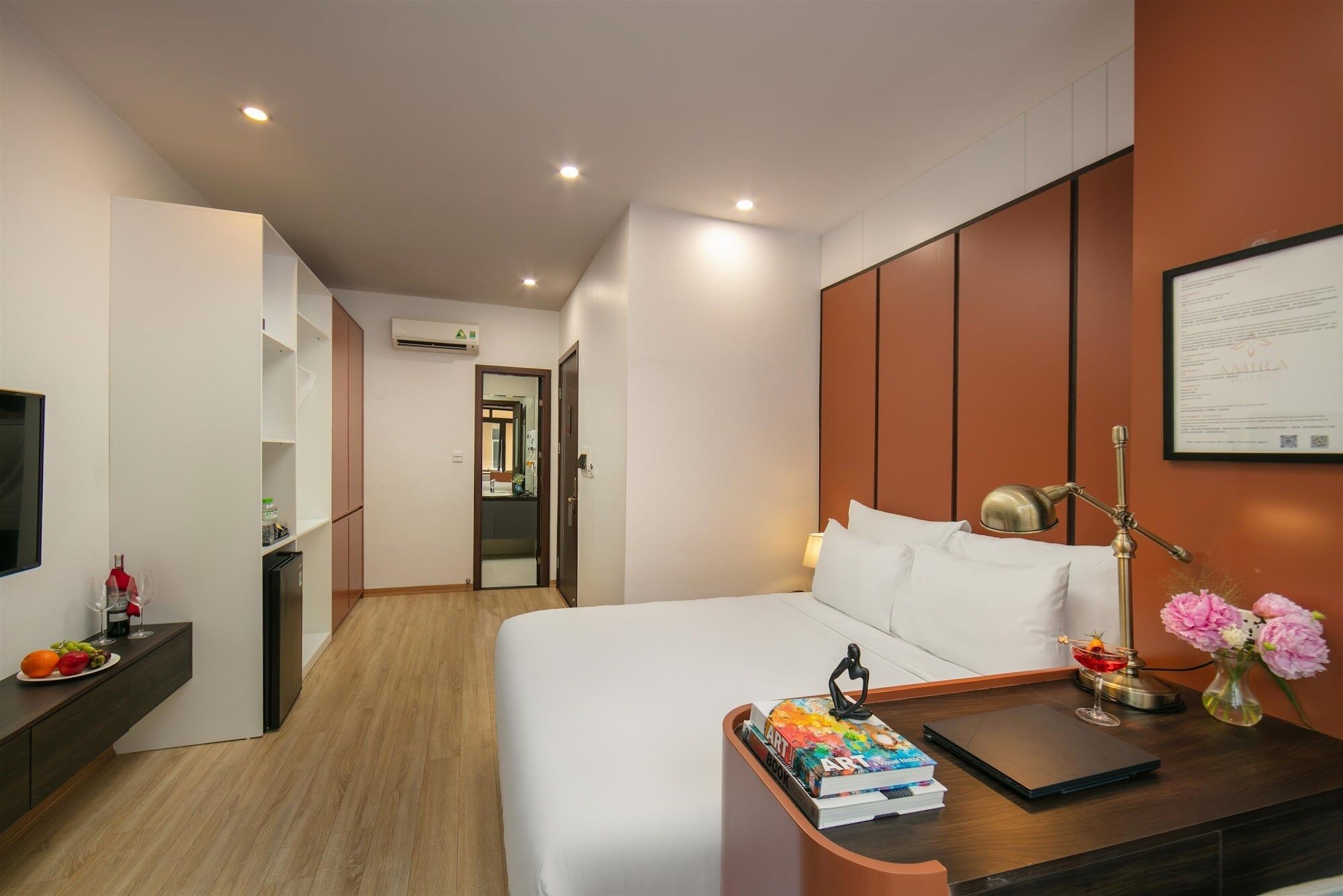 A hotel room with a bed, bedside table, lamp, and a view of the hallway.
