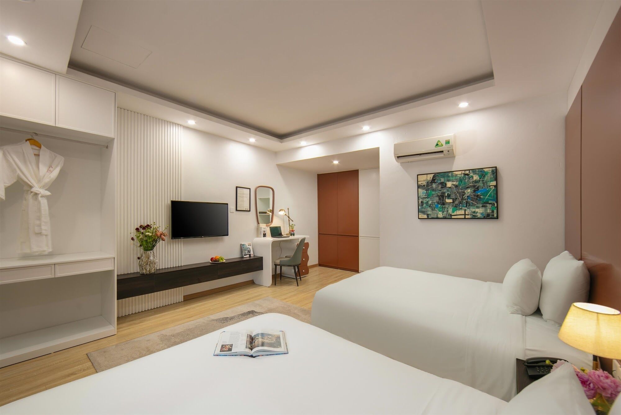 A hotel room with two beds, a TV, a desk, a mirror, and a painting on the wall.