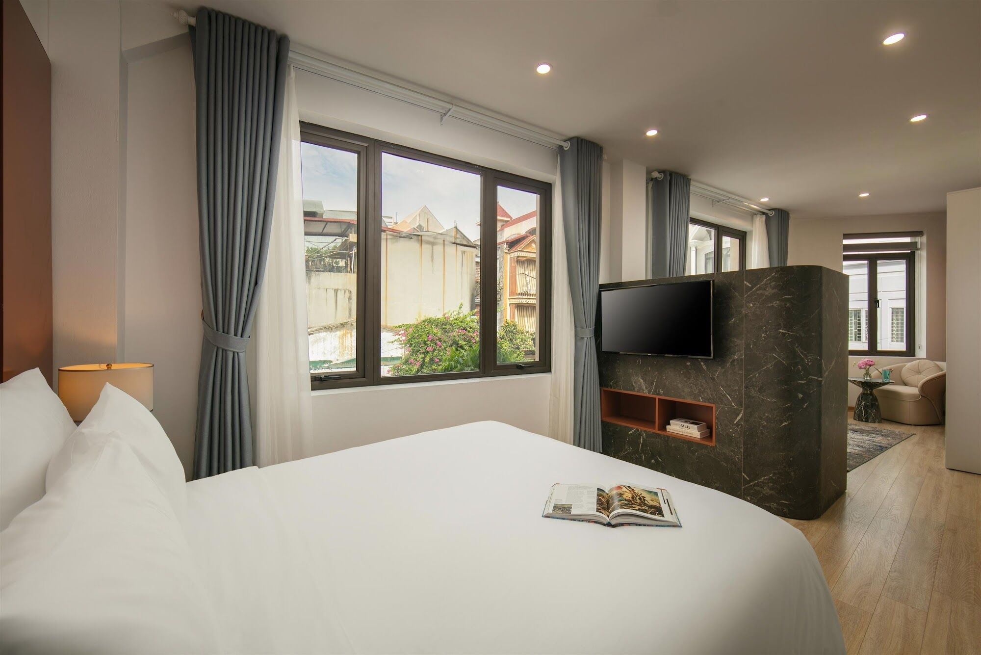 A hotel room with a large bed, a TV mounted on a marble wall, and a view of the outside.