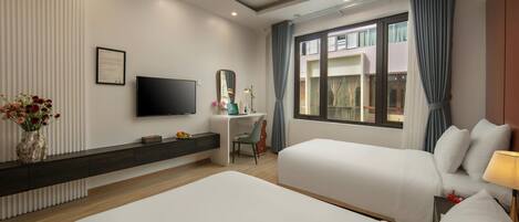 Habitación de hotel con dos camas, un escritorio con silla, televisor de pantalla plana, ventana grande con cortinas y un florero con flores.