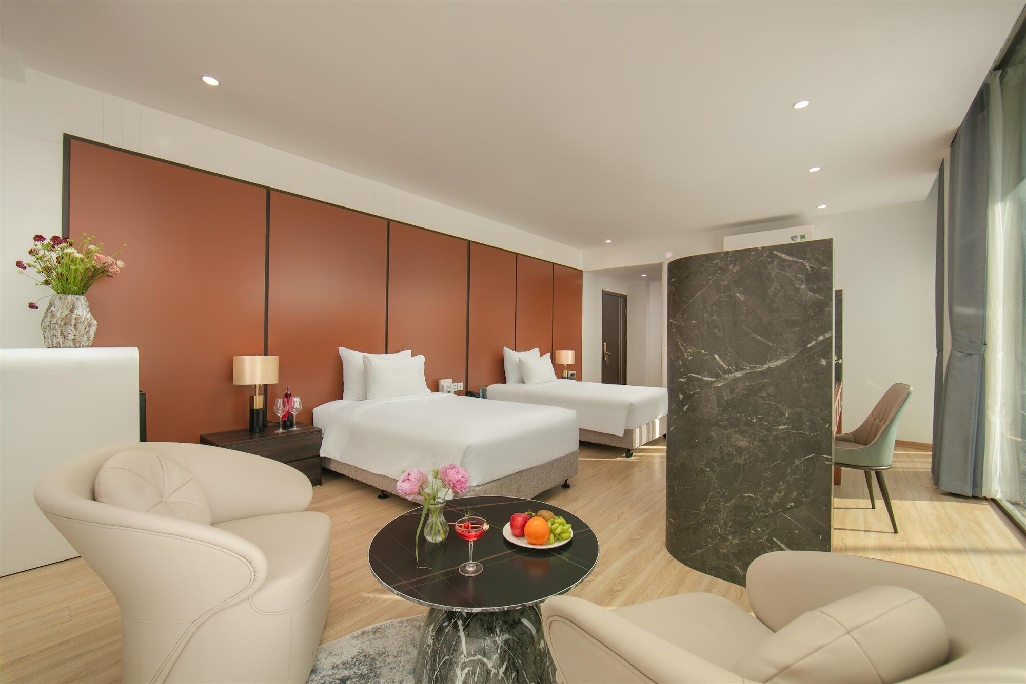 A modern hotel room with two beds, a sitting area with a table, and a large window.