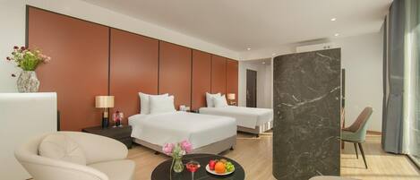 A modern hotel room with two beds, a sitting area with a table, and a large window.