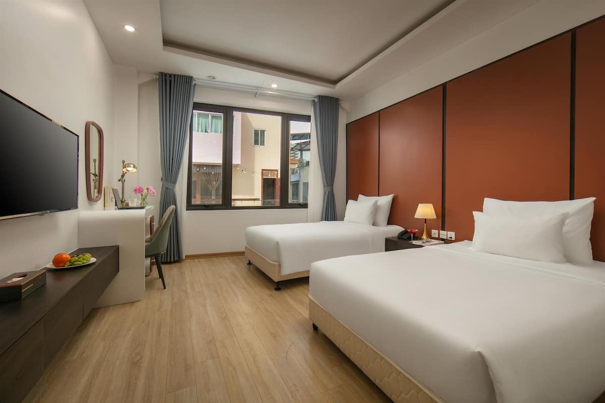 Une chambre d’hôtel avec deux lits, un bureau avec une chaise, une télévision et une fenêtre avec des rideaux.