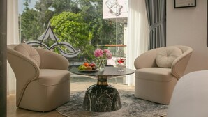 Una sala de estar moderna con dos sillones color beige, una mesa de centro con tapa de vidrio y base de mármol, y vista a zonas verdes.