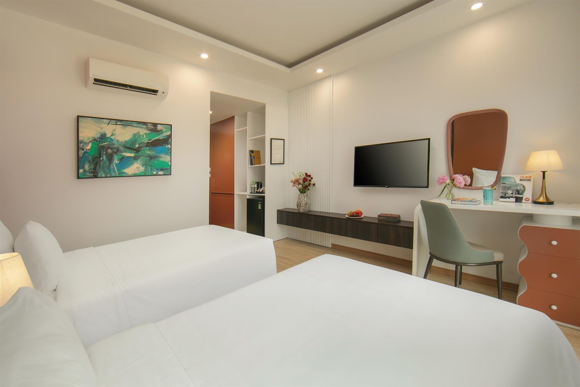 A hotel room with two beds, a desk with a chair, a TV, a bookshelf, and a painting on the wall.