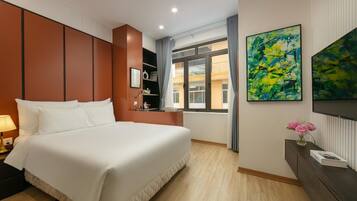 Hotelkamer met een bed, nachtkastje, bureau met lamp, raam met gordijnen en abstracte schilderijen aan de wanden.