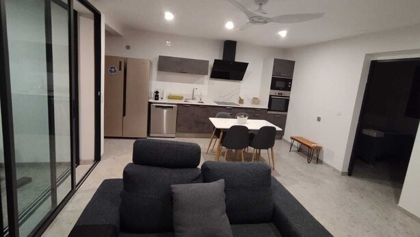 A modern living area with a sofa, dining table, and chairs. There is a kitchen in the background with cabinets and a stove. - Cosy, comfortable villa 15 minutes from the sea (Saint-Pierre)