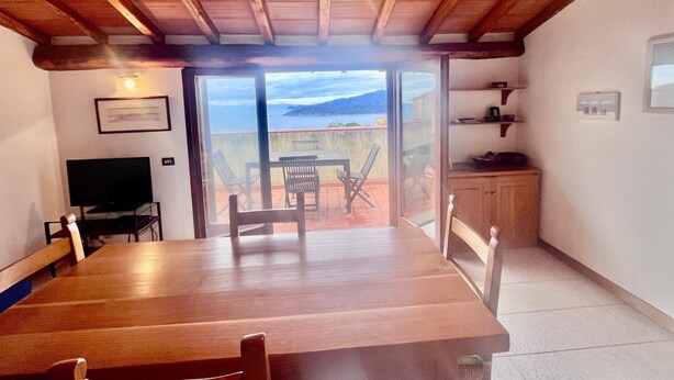 Un comedor con una mesa y sillas de madera, un televisor y vista al mar a través de un ventanal.