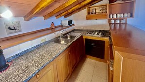 Una cocina con armarios de madera, encimeras de granito, un fregadero, una estufa y un microondas.