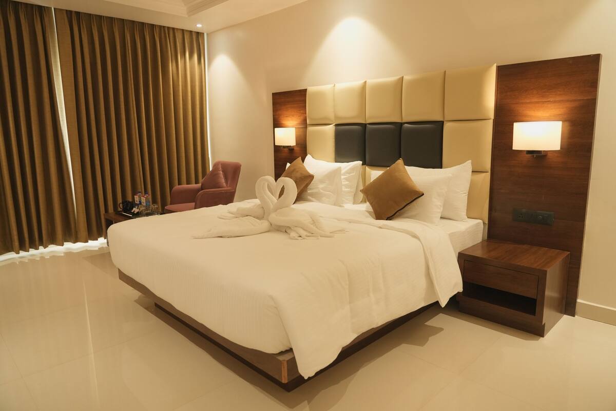 Quarto de hotel com uma cama grande, uma mesa de cabeceira, uma cadeira e um abajur.