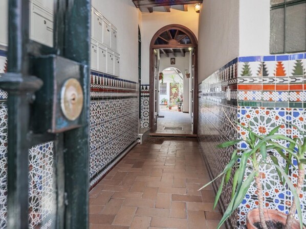 A corridor with patterned tiles, a door with a lock, and a potted plant.