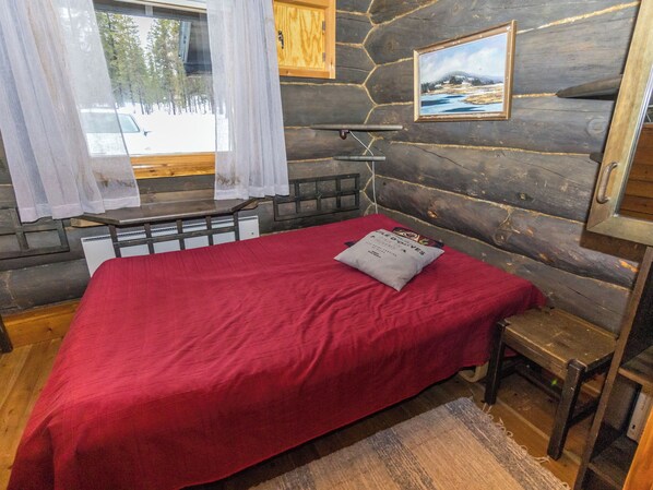 A log cabin room with a bed, a bench, a window with curtains, a painting on the wall, and a wooden door. - Villa kopararova by Interhome (Inari)