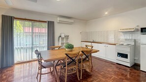 A modern kitchen with white cabinets, a stove, and a microwave. There is a dining area with a wooden table and chairs, and a potted plant on the table. - Canyon Walk House and Unit - Located in the heart of Bright (Bright)
