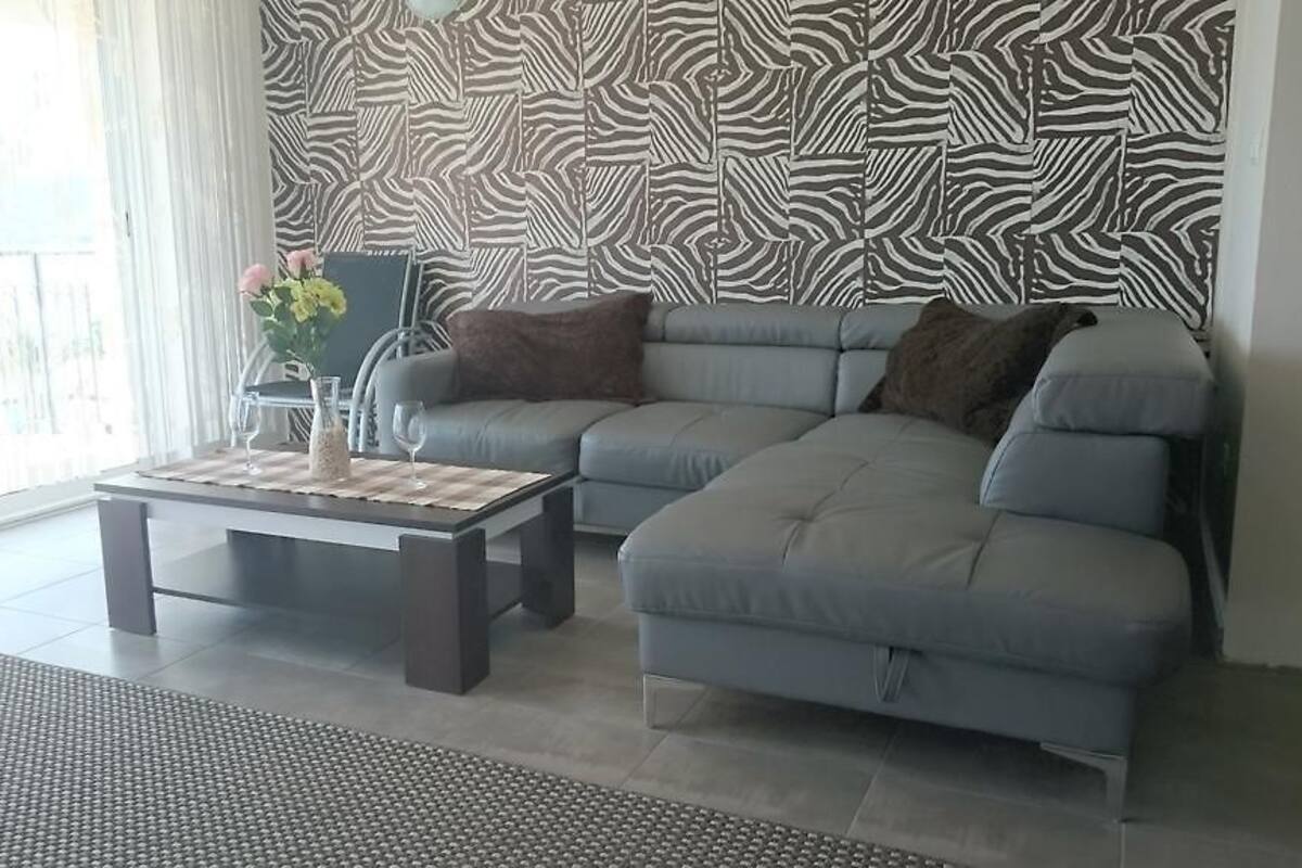 A living room with a grey sofa, a coffee table, and a patterned wallpaper.