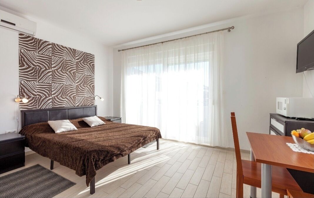 A hotel room with a bed, bedside tables, a desk with a chair, a television, and a window with curtains.