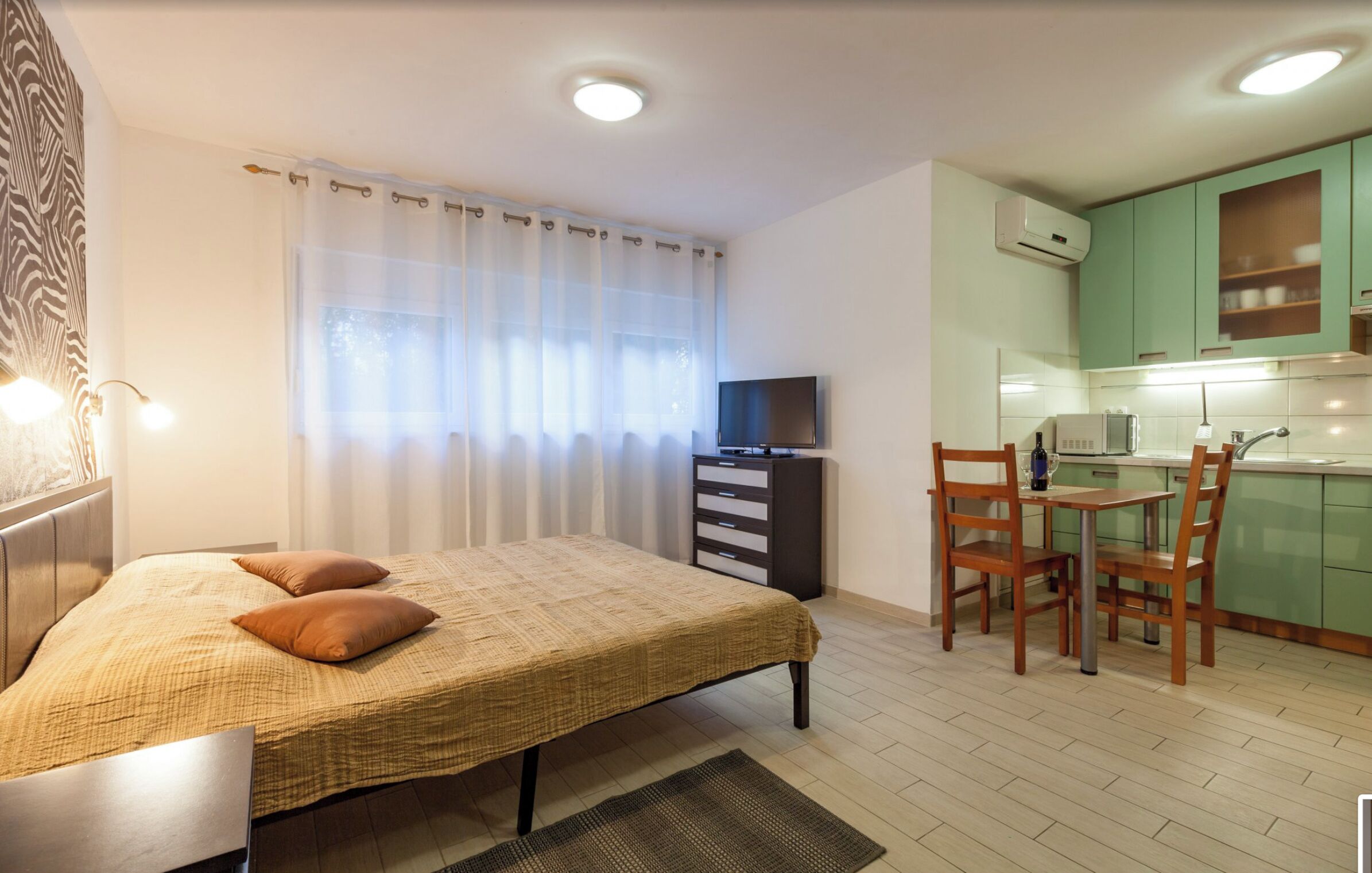 Een slaapkamer met een bed, een televisie en een kitchenette met groene kastjes en een magnetron.