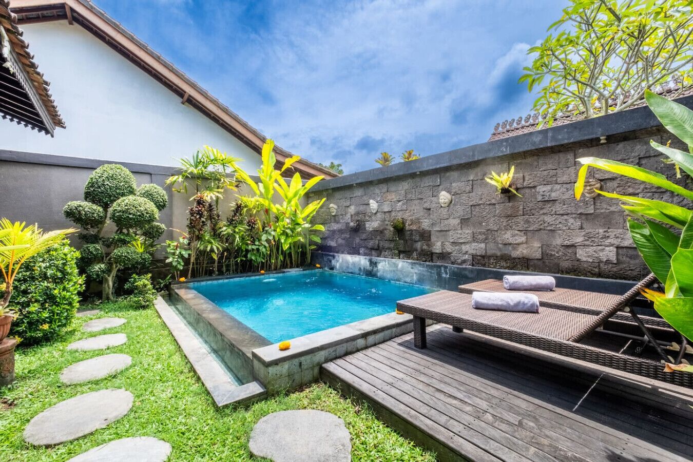 A private pool area with a hot tub, lounge chairs, and a stone wall with decorative elements.