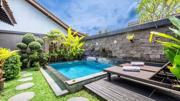 A private pool area with a hot tub, lounge chairs, and a stone wall with decorative elements.