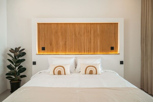 A hotel room with a wooden headboard, white bedding, and a potted plant.