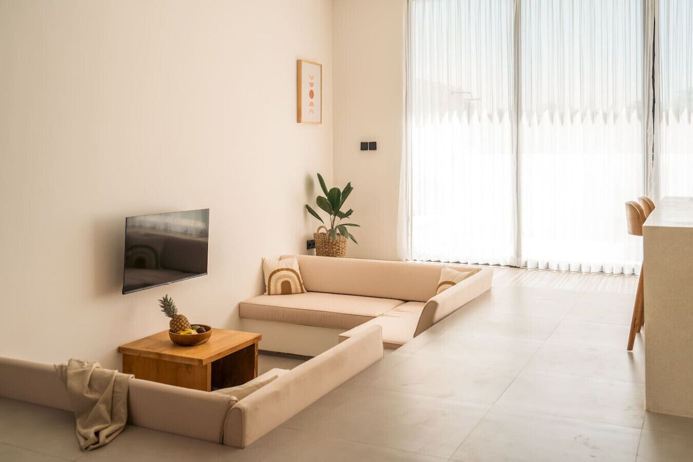 Ein modernes Wohnzimmer mit einer Couch, einem Flachbildfernseher, einem kleinen Holztisch mit Obst und einer Topfpflanze.