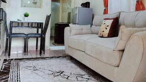 Una sala de estar con un sofá, una mesa de comedor con sillas, un refrigerador y un adorno en la pared.