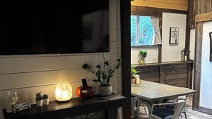 Een moderne woonkamer met een stenen openhaard, een flatscreen televisie erboven en een eethoek met een houten tafel en stoelen.