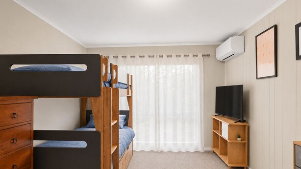 Une chambre avec des lits superposés, une télévision, un petit meuble et une fenêtre avec des rideaux.