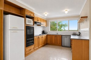 A modern kitchen with wooden cabinets, a refrigerator, microwave, oven, and dishwasher. - Island Treetops by Ready Set Stay (Smiths Beach)