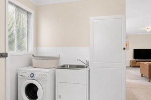 A laundry area with a washing machine, a dryer, and a sink. - Island Treetops by Ready Set Stay (Smiths Beach)