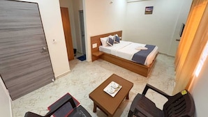 Habitación de hotel con cama, una mesita con una bandeja de objetos, dos sillas, un ventilador de techo y una puerta.