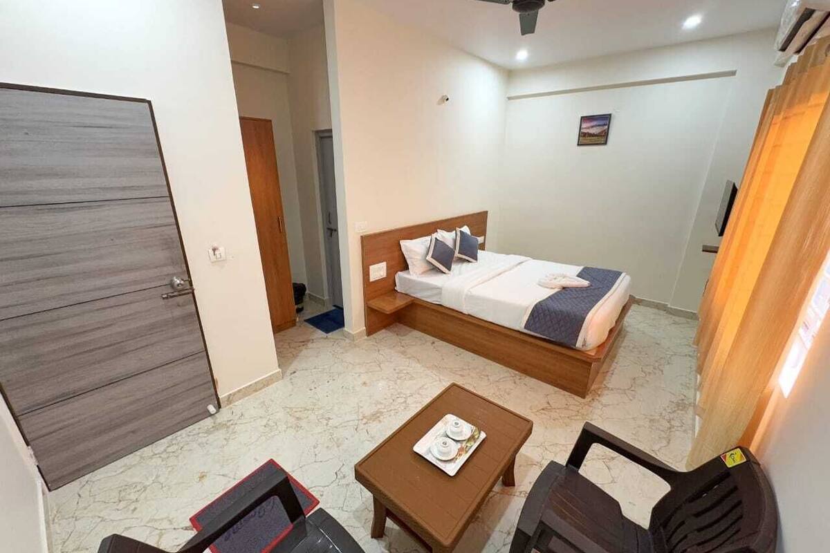Ein Hotelzimmer mit einem Bett, einem kleinen Tisch mit Tablett, zwei Stühlen, einem Deckenventilator und einer Tür.