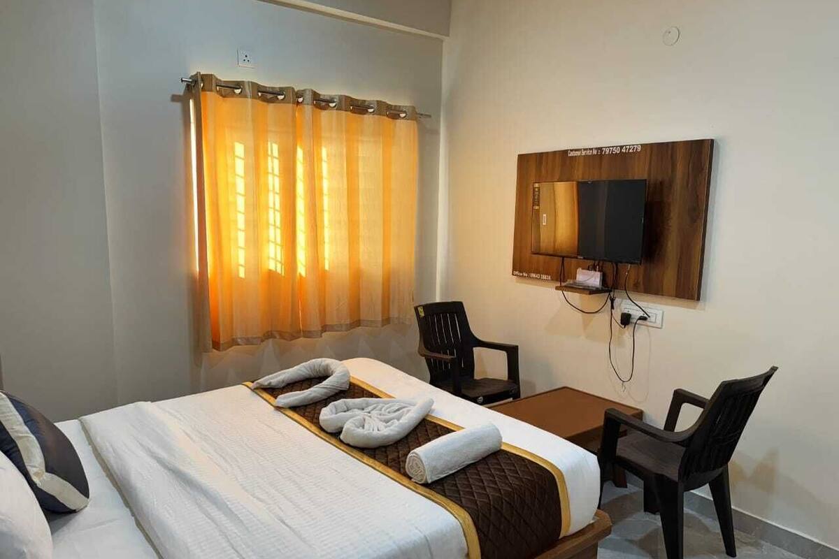 Ein Hotelzimmer mit Bett, Schreibtisch, zwei Stühlen, Fernseher und einem fenster mit Vorhängen.