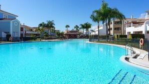 Piscina azul cristalina rodeada de edificios con balcones, palmeras y un cielo despejado.