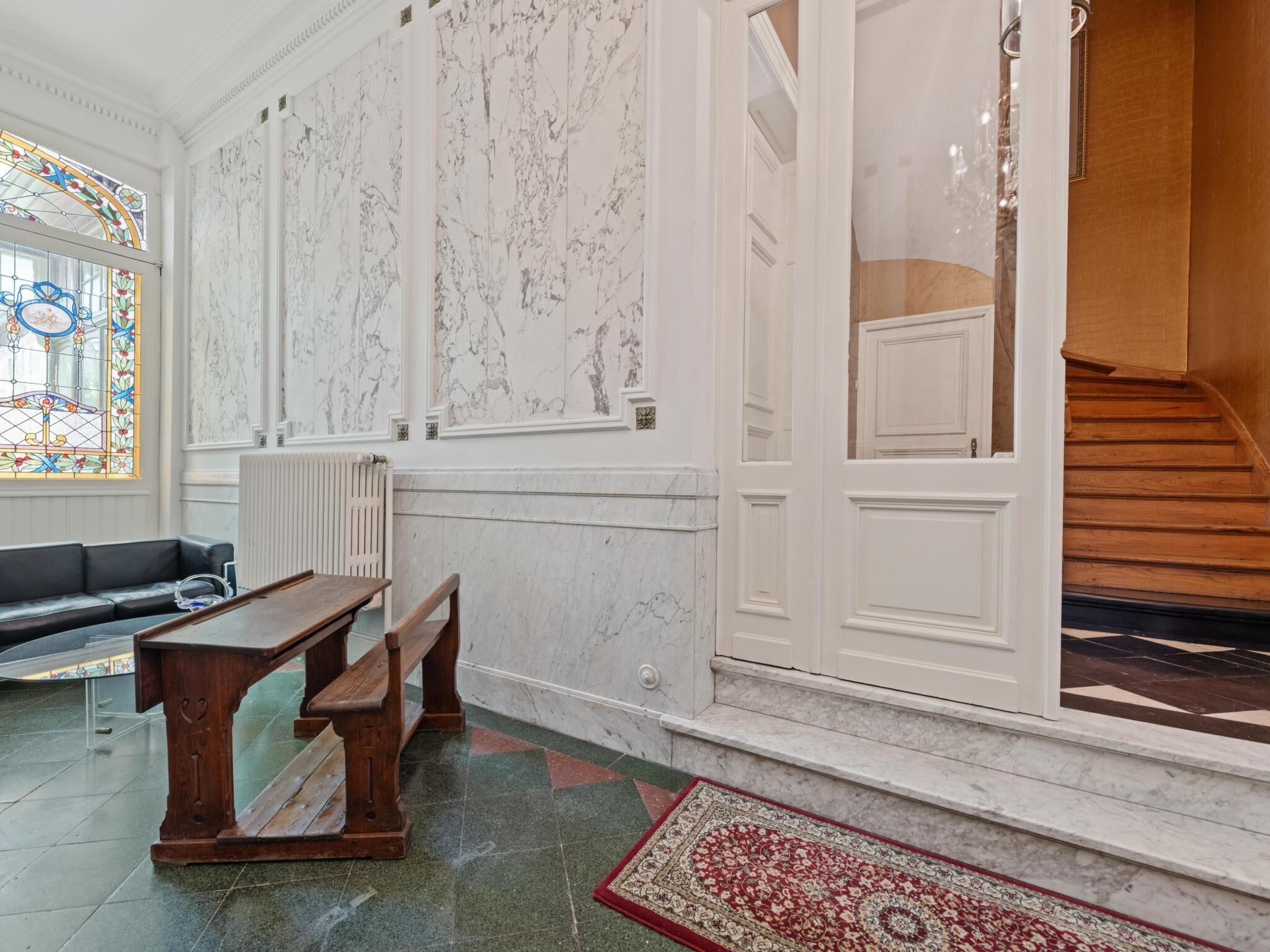 A room with a marble wall, a wooden bench, a red carpet, and a staircase.