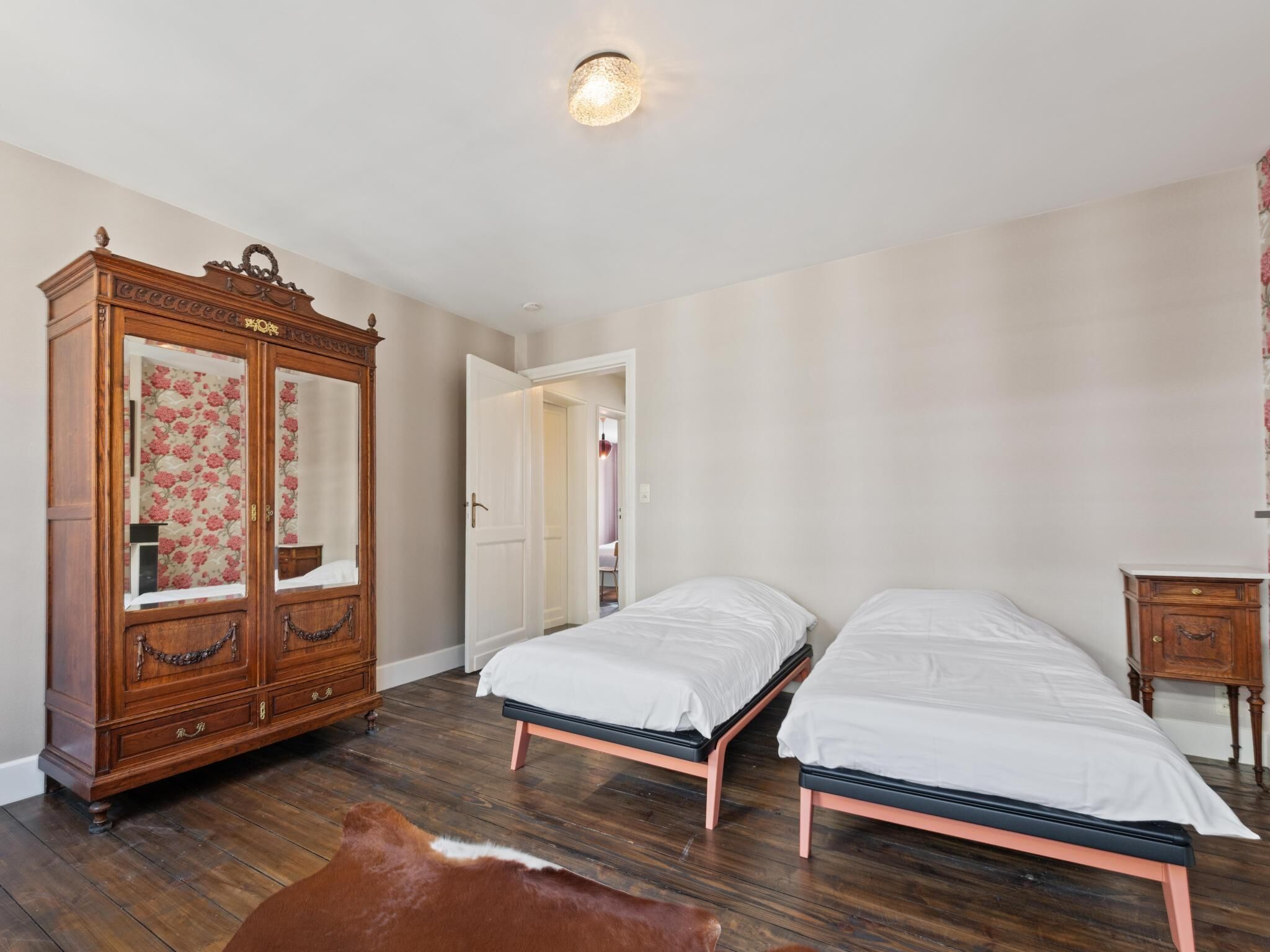 Un dormitorio con dos camas, un armario de madera y un tapete de cuero de vaca.