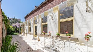 Un bâtiment à la façade en briques, doté de grandes fenêtres et de plantes en pot posées sur le rebord des fenêtres.