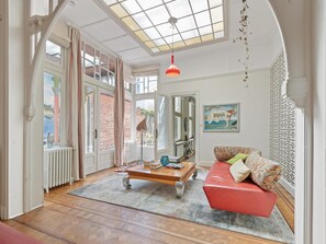 A spacious room with a large window, a red sofa, a wooden coffee table, and a hanging light fixture.