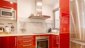 Une cuisine moderne avec des meubles de rangement rouges, des appareils en acier inoxydable, notamment un four à micro-ondes, un four et un réfrigérateur, ainsi qu’une machine à café posée sur le plan de travail.