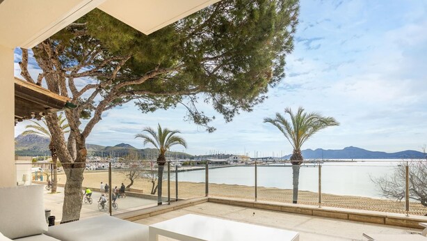 Un espace extérieur moderne, aménagé avec des meubles blancs, offrant une vue sur une marina et une plage.