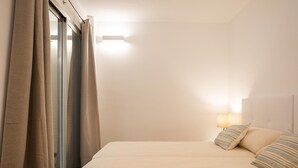 Une chambre à coucher avec un lit, des oreillers, une table de chevet, une lampe et une fenêtre avec des rideaux.